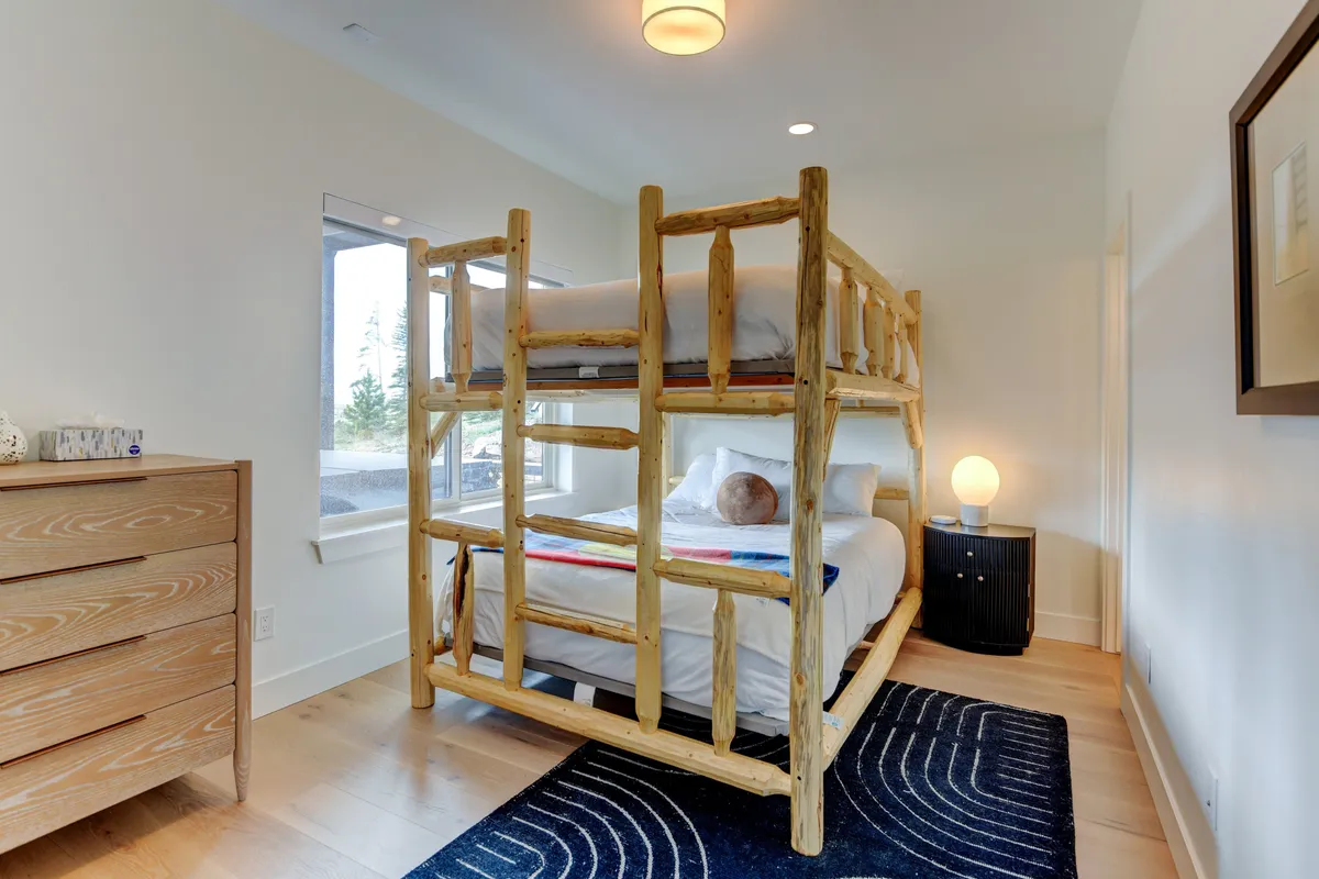 A playful and comfortable bunk room with a sturdy bunk bed, dresser, and nightstand. Soft bedding, area rug, and playful touches make this space ideal for kids or groups, offering both fun and relaxation. The lighting and decor are warm and inviting.