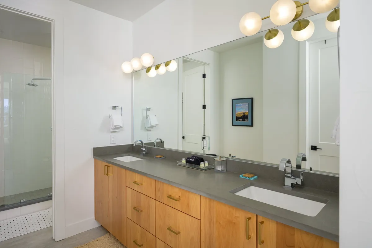 A modern, spa-inspired bathroom with a double vanity sink, large mirror, decorative lighting, and framed artwork. The space feels fresh and inviting, offering guests a luxurious area for morning routines or evening relaxation.