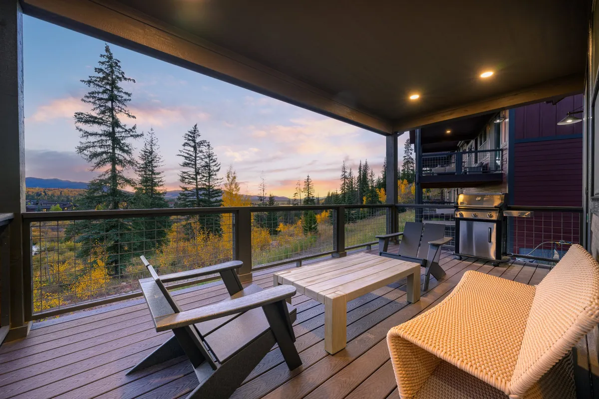 This exterior image features an inviting outdoor seating area with a grill, comfortable furnishings, and a breathtaking view of distant mountains beneath a vibrant sunset sky. The setup suggests opportunities for relaxing, dining, and socializing outdoors while enjoying the natural surroundings.