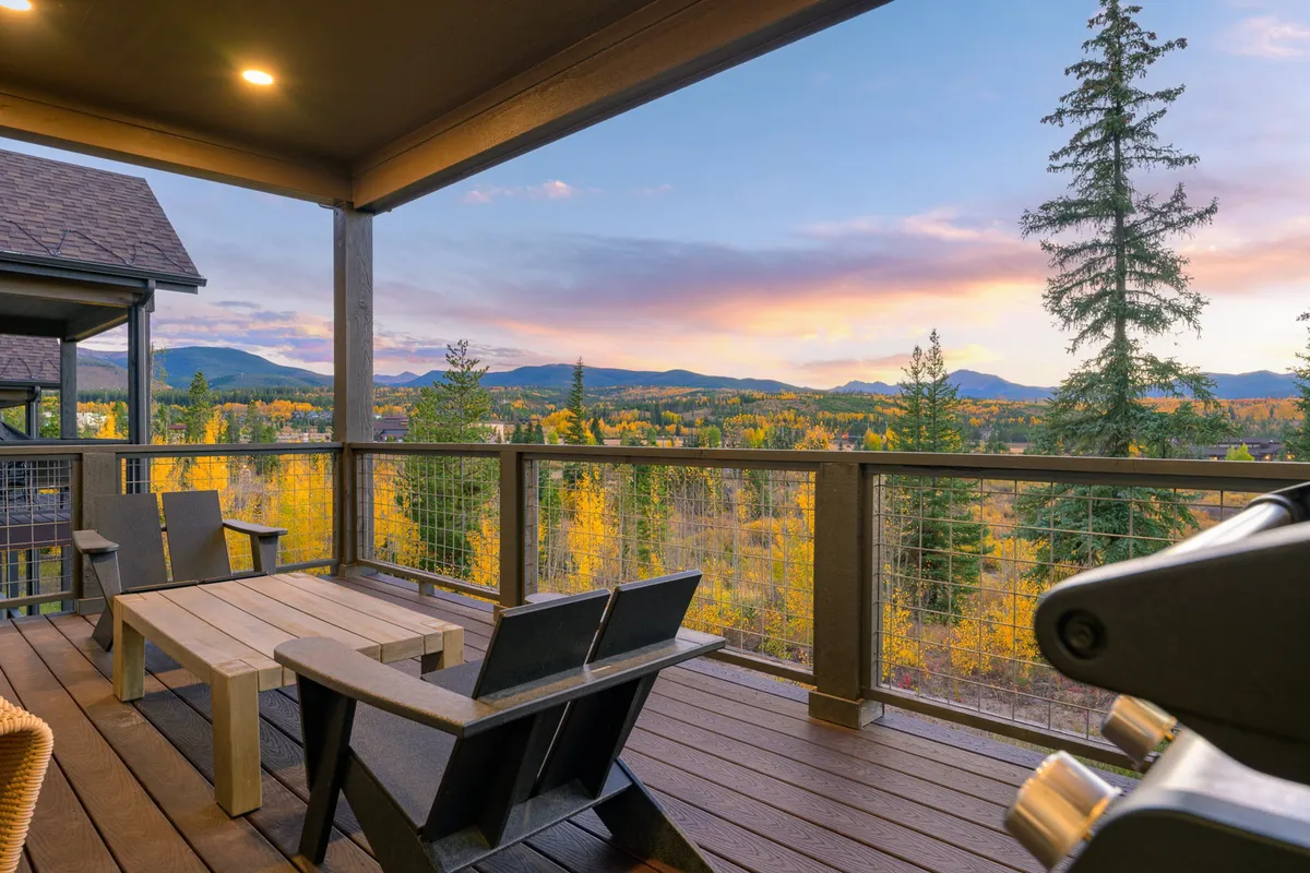 A serene covered deck with adjoining chairs and a wooden table, overlooking a scenic expanse of mountains and trees. The space is perfect for sipping coffee, relaxing, or enjoying gentle breezes and sunsets.