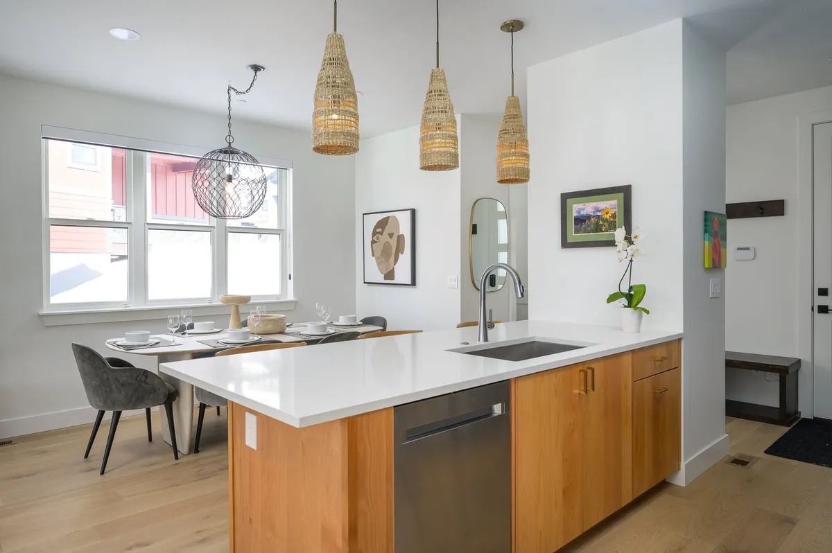 An inviting open-concept kitchen and dining space, showcasing a kitchen island with hanging pendant lights, a large dining table beautifully set for a meal, and contemporary artwork on the walls. The layout encourages togetherness, ideal for family feasts or casual breakfasts.
