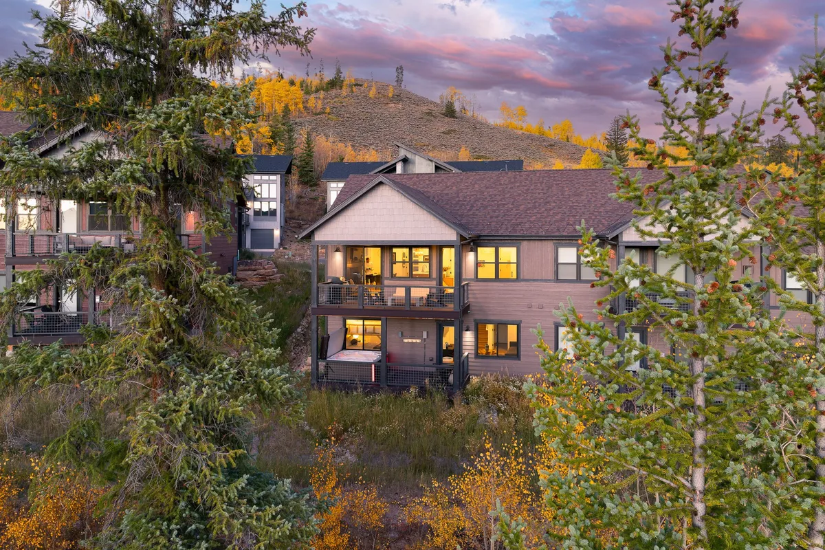 The home's balcony overlooks a vibrant autumn landscape, with surrounding trees and a colorful sunset sky. The inviting setup highlights outdoor living and easy access to nature trails.