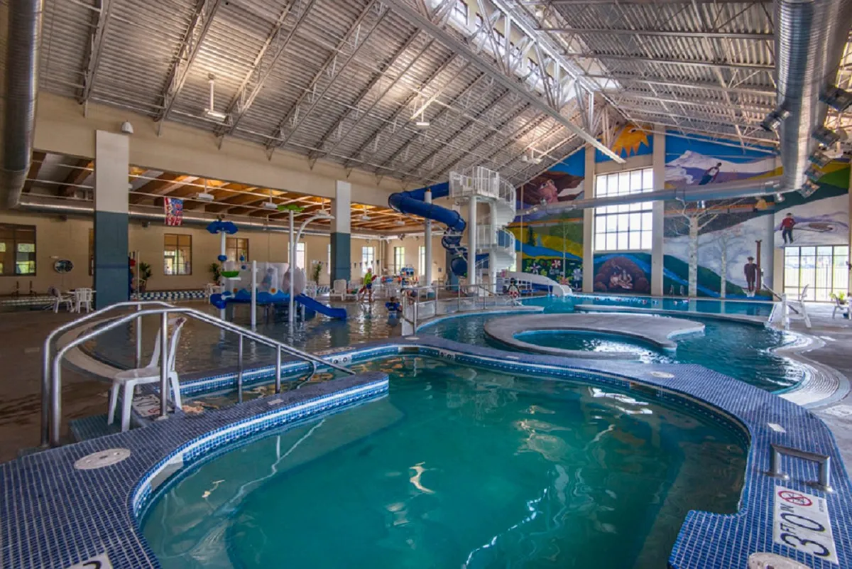 This vibrant interior shot captures the Grand Park Rec Center’s aquatic area, featuring a large swimming pool, colorful water slides, playful murals, and children enjoying the water. The scene is full of lively activity and joyful family moments.